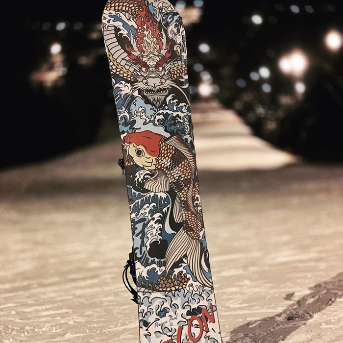 Snowboard standing upright on a snowy slope at night, featuring bold Japanese-inspired artwork of a koi fish swimming through crashing waves beneath a fierce dragon with flames and swirling water patterns.